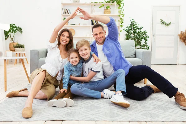 Щаслива сім'я приєднуються руки роблячи символічний дах сидить вдома — стокове фото