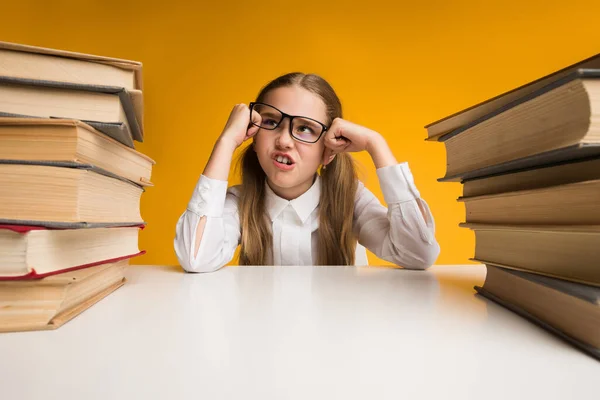 Boos schoolmeisje zit tussen boeken moe van huiswerk, gele achtergrond — Stockfoto