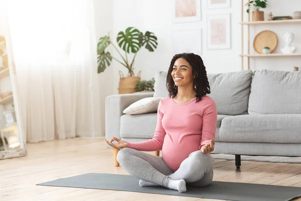 Smiling pregnant black woman sitting in lotus pose at home — Stock Photo, Image