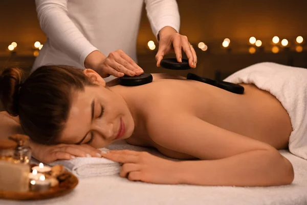 Młoda kobieta otrzymuje masaż gorącymi kamieniami w nowoczesnym spa — Zdjęcie stockowe