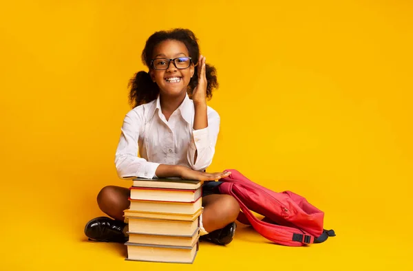 Studentessa africana alzare la mano seduta su libri su sfondo giallo — Foto Stock