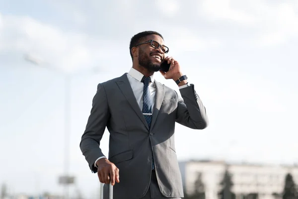 Hombre de negocios hablando en el teléfono celular de pie con la maleta de viaje al aire libre —  Fotos de Stock