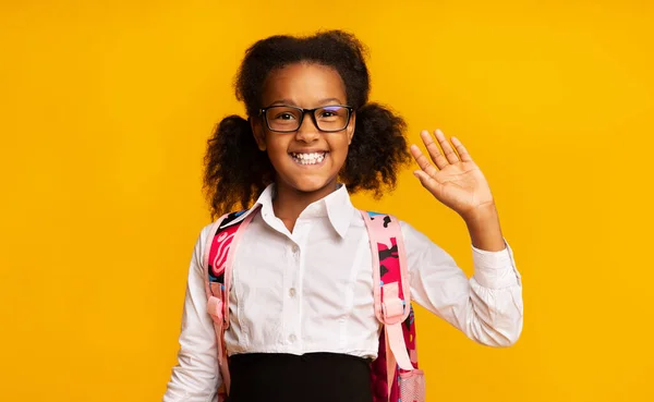 Afrikaans schoolmeisje zwaaien hand groet glimlachen op gele achtergrond — Stockfoto