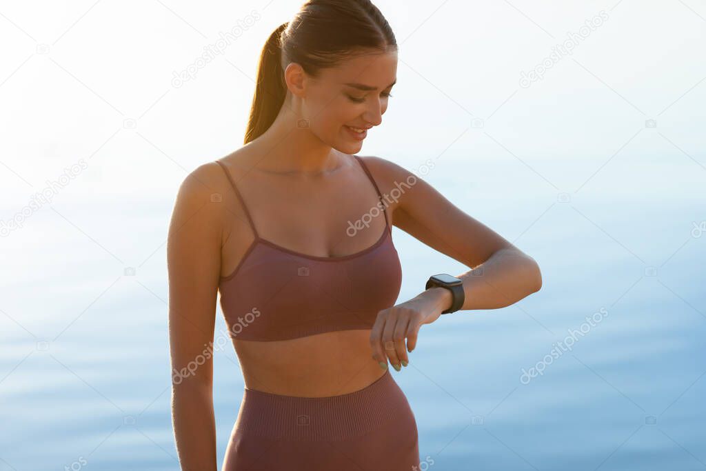 Woman standing on the beach, looking at activity tracker