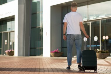 Havaalanı terminalinde bagajlarıyla yürüyen erkek turist.