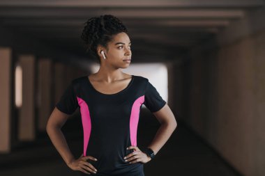 Serious african american girl in sportswear with wireless headphones and fitness tracker