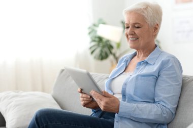 Son sınıflar için başvurular. Evde dinlenirken dijital tablet kullanan yaşlı kadın