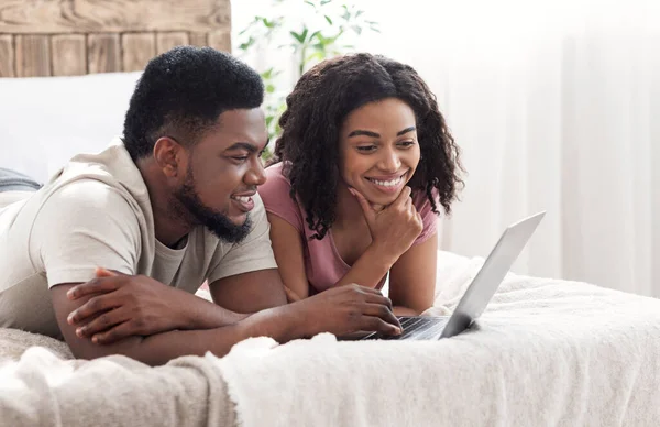 Gli amanti africani positivi che utilizzano il computer portatile insieme, interno della camera da letto — Foto Stock