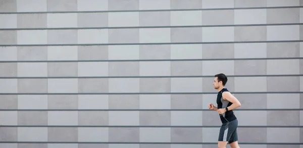Jogging in city. Slender guy in sportswear with fitness tracker, runs — Stock Photo, Image