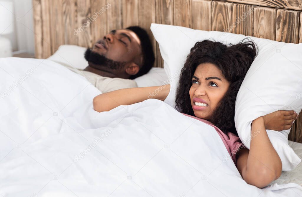 Angry black woman covering her ears with pillow