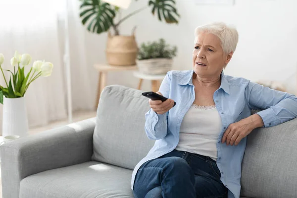 《突发新闻》震惊的老年妇女在家看电视，坐在沙发上 — 图库照片
