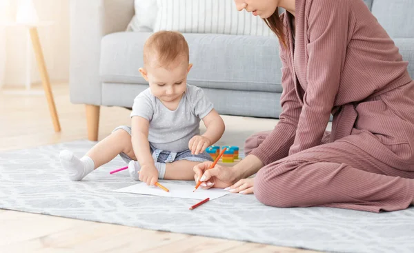 Schattig weinig baby tekenen met potloden op de vloer met zijn moeder — Stockfoto