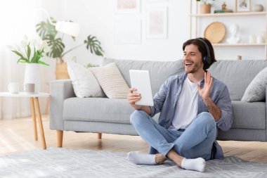 Evde dijital tablet kullanan, video görüşmesi yapan olumlu bir adam.