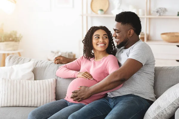 Прекрасні щасливі очікування африканських батьків сидять на дивані вдома — стокове фото