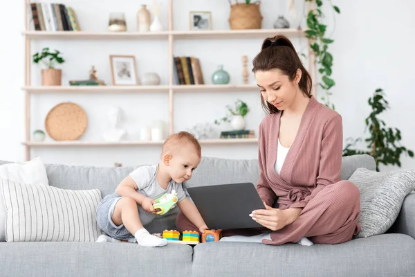 Cours en ligne pour mamans. Jeune femme étudiant avec ordinateur portable à côté de bébé — Photo