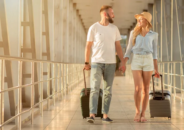 Happy couple walking in airport with luggage