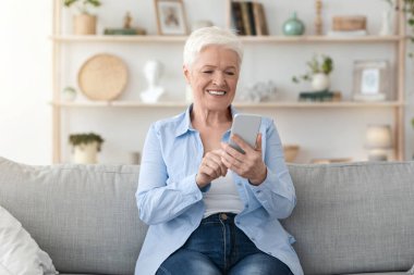 Kolay ödeme uygulaması. Gülümseyen Kıdemli Kadın Evde Modern Akıllı Telefon Kullanıyor