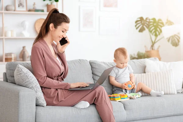 Mamá trabajadora. Mujer joven freelancer usando el teléfono celular y el ordenador portátil al lado del bebé — Foto de Stock