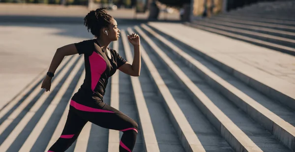 Bom dia. menina afro-americana com fones de ouvido sem fio e rastreador de fitness sobe as escadas — Fotografia de Stock