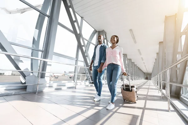Romántica pareja africana caminando con maletas hasta la puerta de embarque en el aeropuerto — Foto de Stock