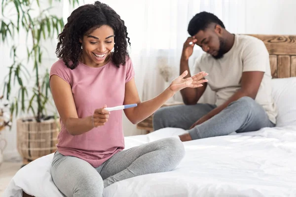 Opgewonden zwarte vrouw met zwangerschap test naast gefrustreerde man — Stockfoto