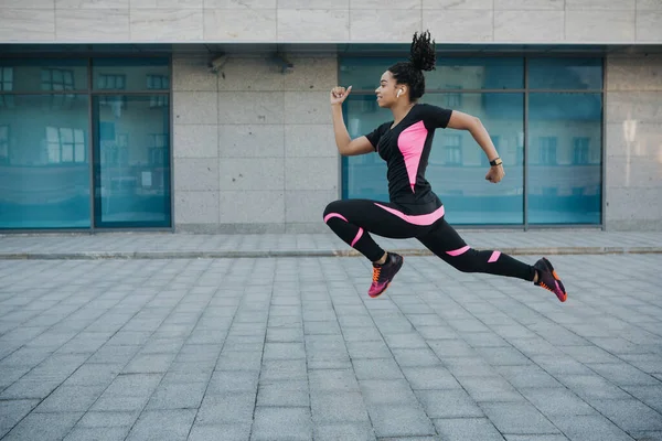 Exercício para perda de peso. Mulher em sportswear com fones de ouvido sem fio congelados no ar, pulando enquanto corre — Fotografia de Stock