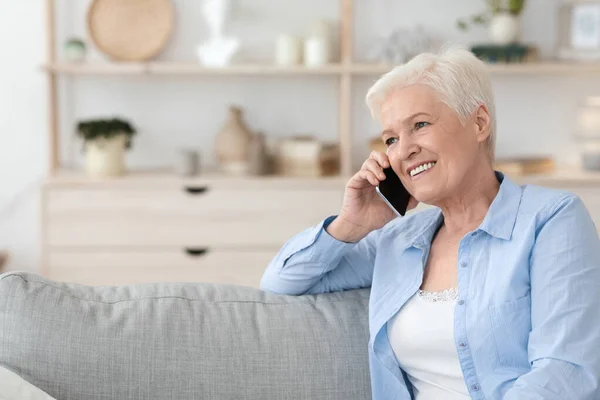 Улыбающаяся пожилая леди разговаривает по телефону, расслабляясь дома на диване — стоковое фото