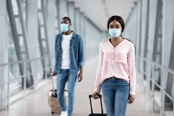 Precauciones de viaje al aeropuerto. Hombre y mujer con máscaras médicas caminando en la terminal —  Fotos de Stock
