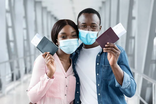 Viaje seguro. Pareja negra con máscaras médicas posando con pasaportes en el aeropuerto —  Fotos de Stock