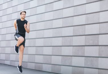 Sokakta koşuyor. Spor giyimli ve spor ayakkabılı genç adam zıplıyor ve koşuyor.