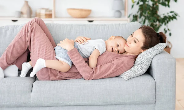 Mutlu anne ve tapılası bebek kanepede uzanıp kucaklaşıyorlar. — Stok fotoğraf