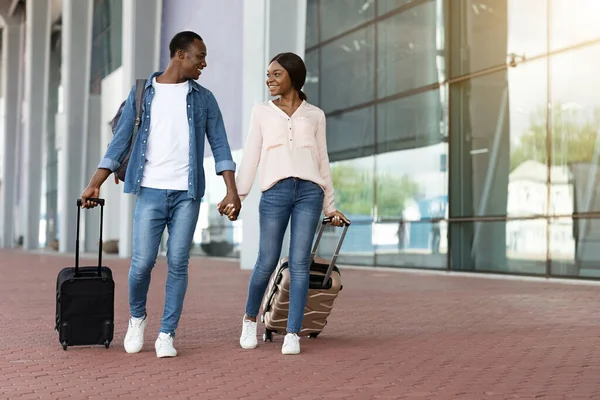 Listo para viajar. Feliz pareja negra caminando con equipaje cerca del edificio del aeropuerto — Foto de Stock