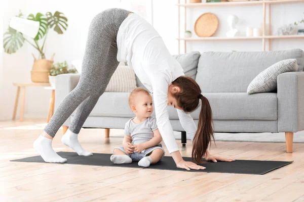 Jovem mãe praticando ioga em casa com o filho pequeno, fazendo exercício de alongamento de volta — Fotografia de Stock
