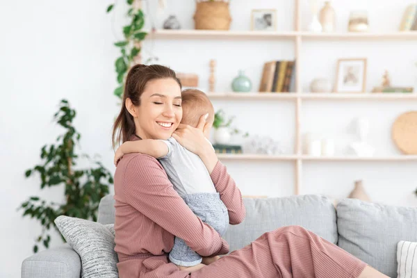 Conexión madre-hijo. Feliz mamá abrazando a su bebé mientras se relaja en el sofá — Foto de Stock