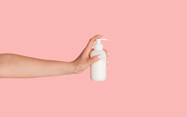 Fechar a mão feminina mostrando garrafa dispensador com produto cosmético sobre fundo rosa — Fotografia de Stock