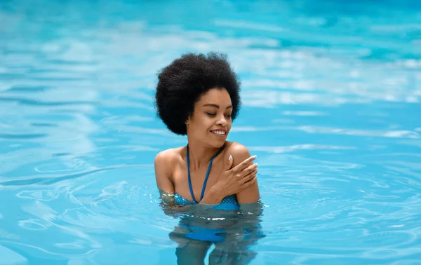 Cheerful black girl in blue bikini swimming at pool in summertime Royalty Free Stock Images