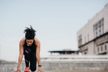 Spor müsabakalarından önce antrenman. Spor kıyafetlerine odaklanmış spor ayakkabılı bir kız başlangıç noktasında duruyor.
