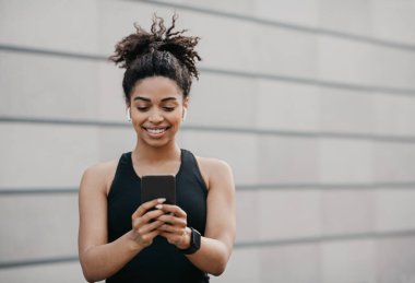 Harika bir ruh hali, müzik ve spor. Spor giyim kuşağında spor ayakkabılı mutlu Afro-Amerikan atletizm kızı akıllı telefon kullanıyor.