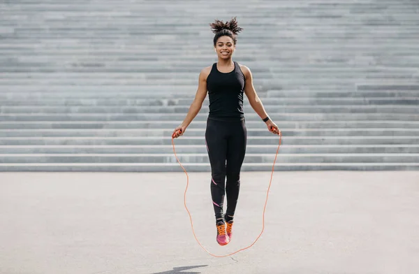 Female athlete does cardio workout. Smiling girl in sportswear with fitness tracker jumping rope — Stock Photo, Image