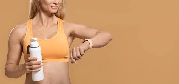 Gesunder Lebensstil, Technologie und Sport. Lächelnde Frau in Sportbekleidung mit Flasche beim Betrachten des Fitness-Trackers, isoliert auf gelbem Hintergrund — Stockfoto