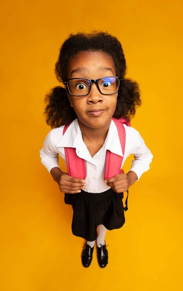 Geschokt Afrikaans schoolmeisje op zoek naar camera staande over gele achtergrond — Stockfoto