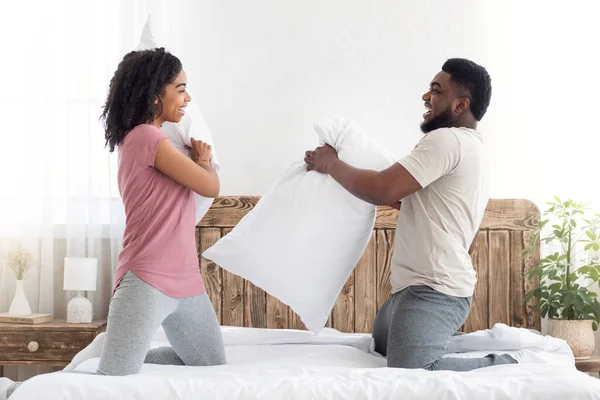 Alegre amoroso casal negro lutando com travesseiros na cama — Fotografia de Stock