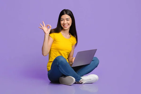 Tudo ok. Joyful menina asiática sentado com laptop e mostrando sinal ok — Fotografia de Stock