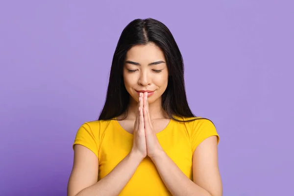 Спокойная азиатская девушка молится, прижав руки к лицу и закрыв глаза — стоковое фото