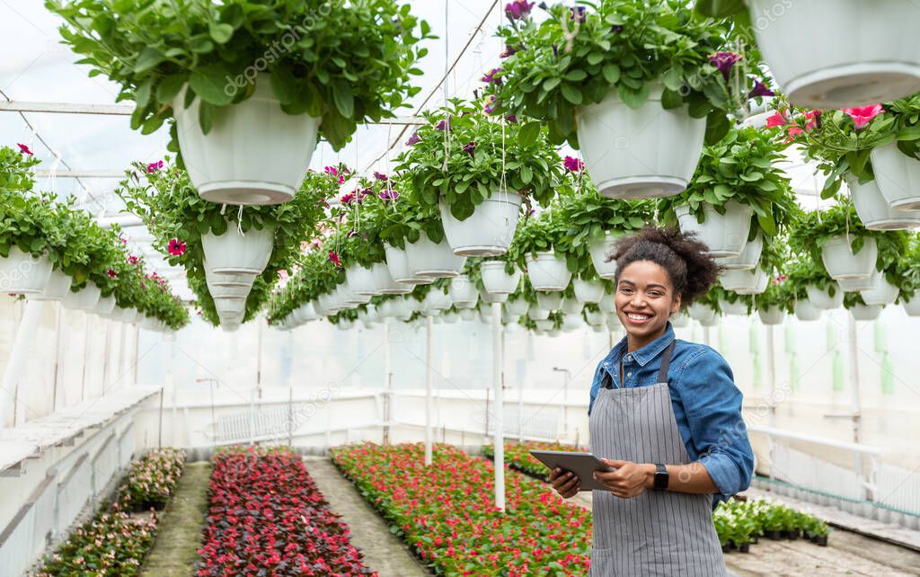 Gardener using digital tablet in greenhouse. Smiling girl with smart watch and tablet, in orangery