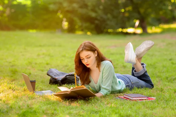 Piękna uczennica przygotowująca się do egzaminów na świeżym powietrzu, leżąca na trawniku z książką — Zdjęcie stockowe