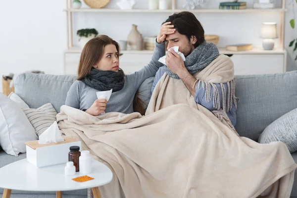 Sjuka par inbäddade i filt sitter på soffan, har feber — Stockfoto