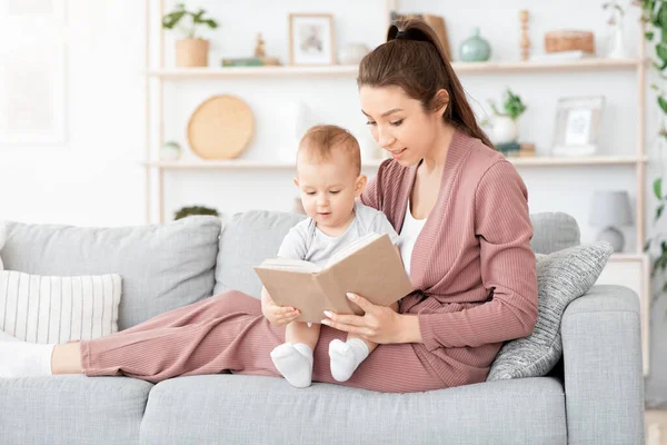 Genç anne ve tatlı bebeği evde kitap okuyorlar. — Stok fotoğraf