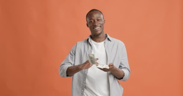 Rikas musta mies heittää rahaa ja nauraa oranssi tausta — kuvapankkivideo
