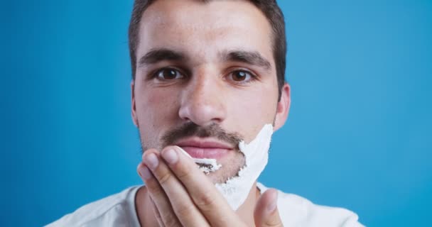 Молодой человек наносит пену для бритья на бороду, крупным планом — стоковое видео